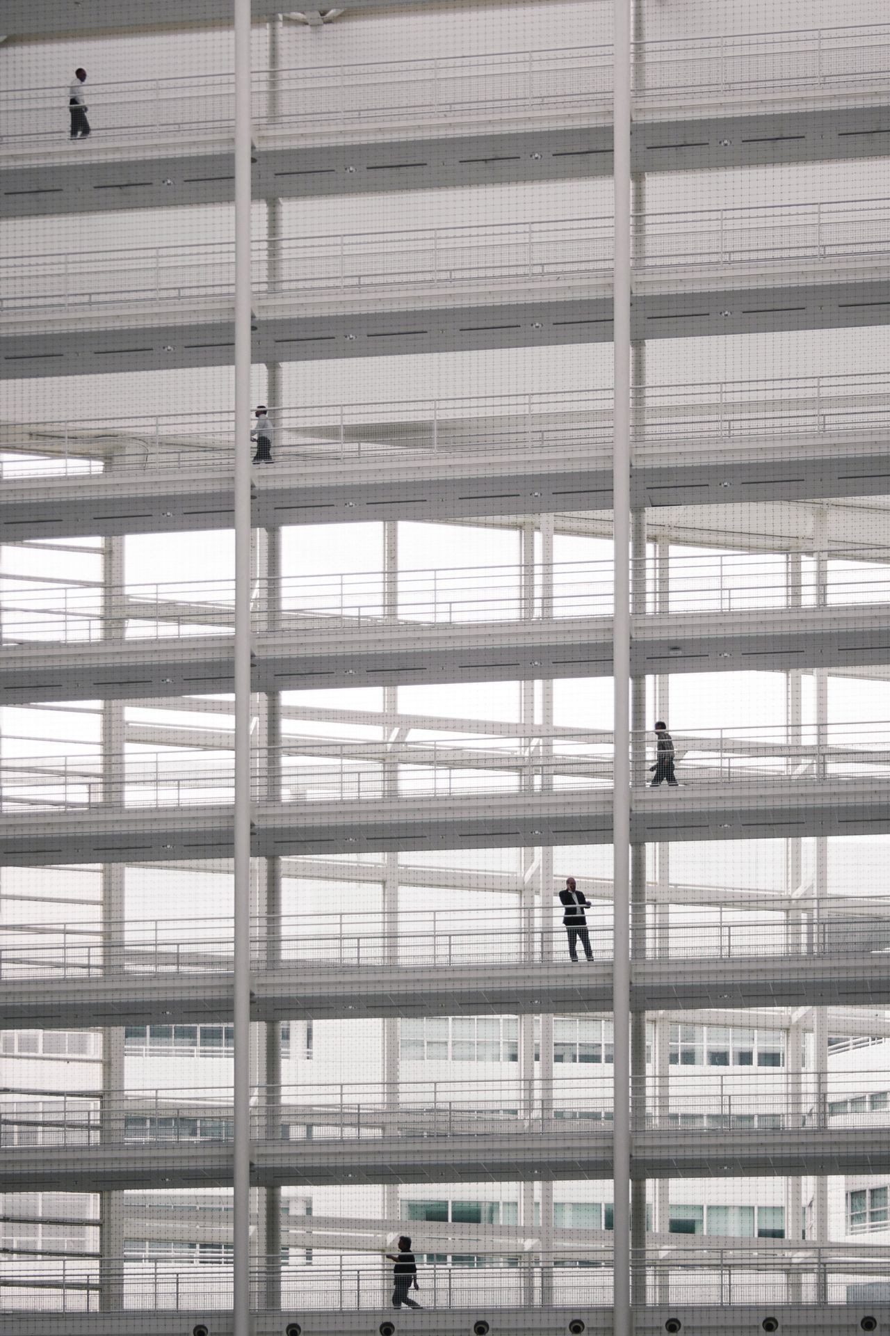 Multiple levels of a building with people walking on different floors, framed by a grid structure.