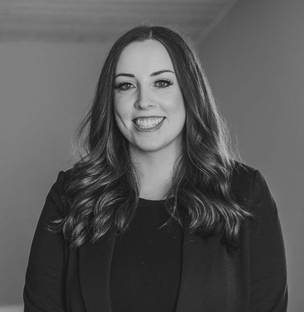 Black and white portrait of a smiling woman with long wavy hair, wearing a blazer.