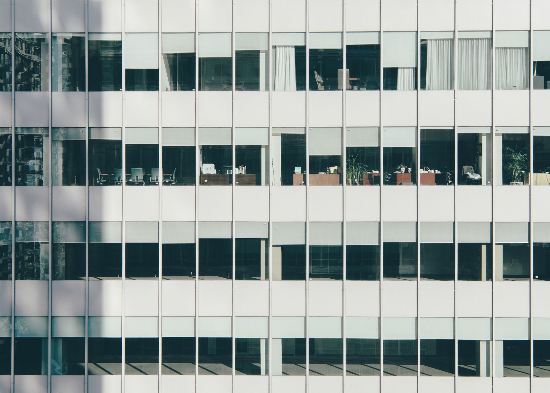 Exterior view of an office building with several desks and chairs visible through large windows.