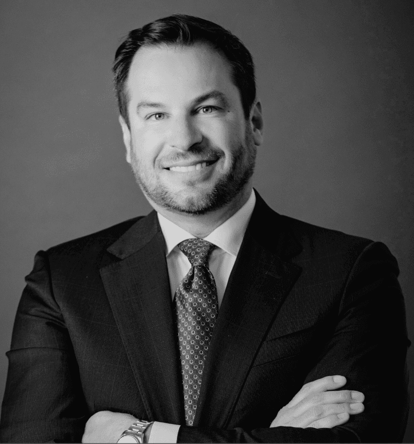 Black and white portrait of a smiling man in a suit and tie with crossed arms.