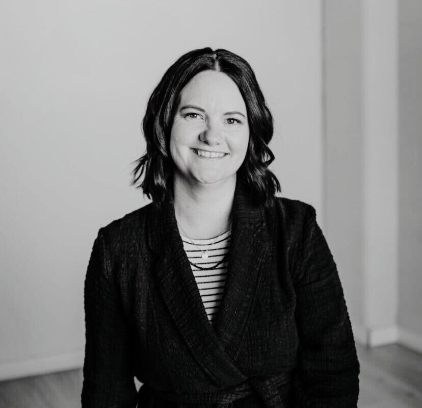 Person wearing a dark jacket over a striped shirt in a minimally decorated room.